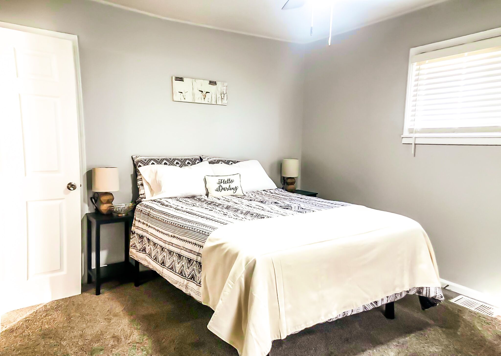 A bedroom with a bed, bedside lamps, a door, and a window with blinds.