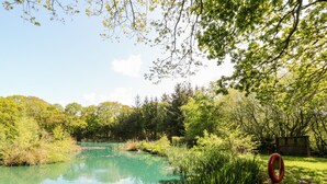 Ein friedlicher Teich, umgeben von üppigem Grün und Bäumen, mit einer Holzsteganlage und einem Schild mit der Aufschrift 'SPRUCE'.