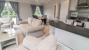 Ein modernes Wohnzimmer mit Sofa, Couchtisch und Essbereich mit Tisch und Stühlen. Es gibt eine Küche mit Herd und Schränken.