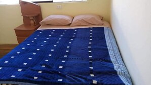 Un dormitorio con una cama, dos almohadas, una mesita de noche de madera y una ventana.