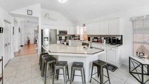 Una cocina moderna con armarios blancos, una isla grande con taburetes de bar y un comedor con cafetera.
