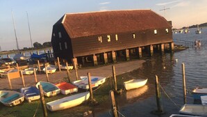 A waterfront property with a large building, several small boats docked on the shore, and a grassy area. - Spacious Refurbished Apartment - 2 mins walk from Bosham Harbour (Bosham)