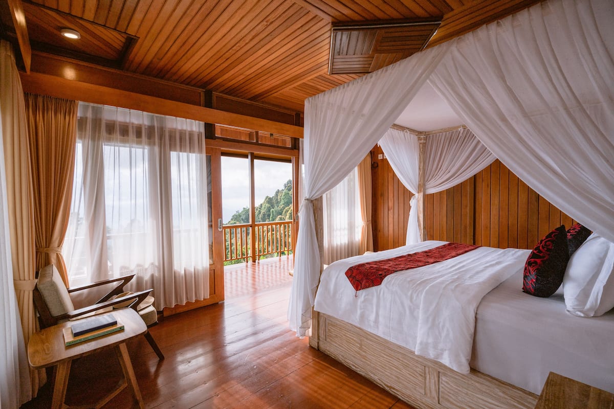 A bedroom with a wooden ceiling, a canopy bed, and a view of a balcony.