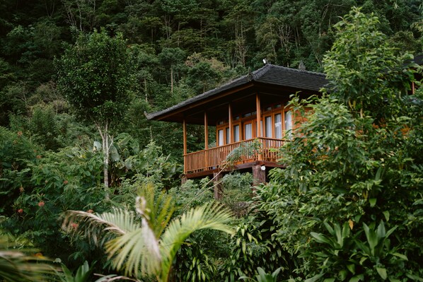 Un edificio de madera con balcón, rodeado de un bosque denso.