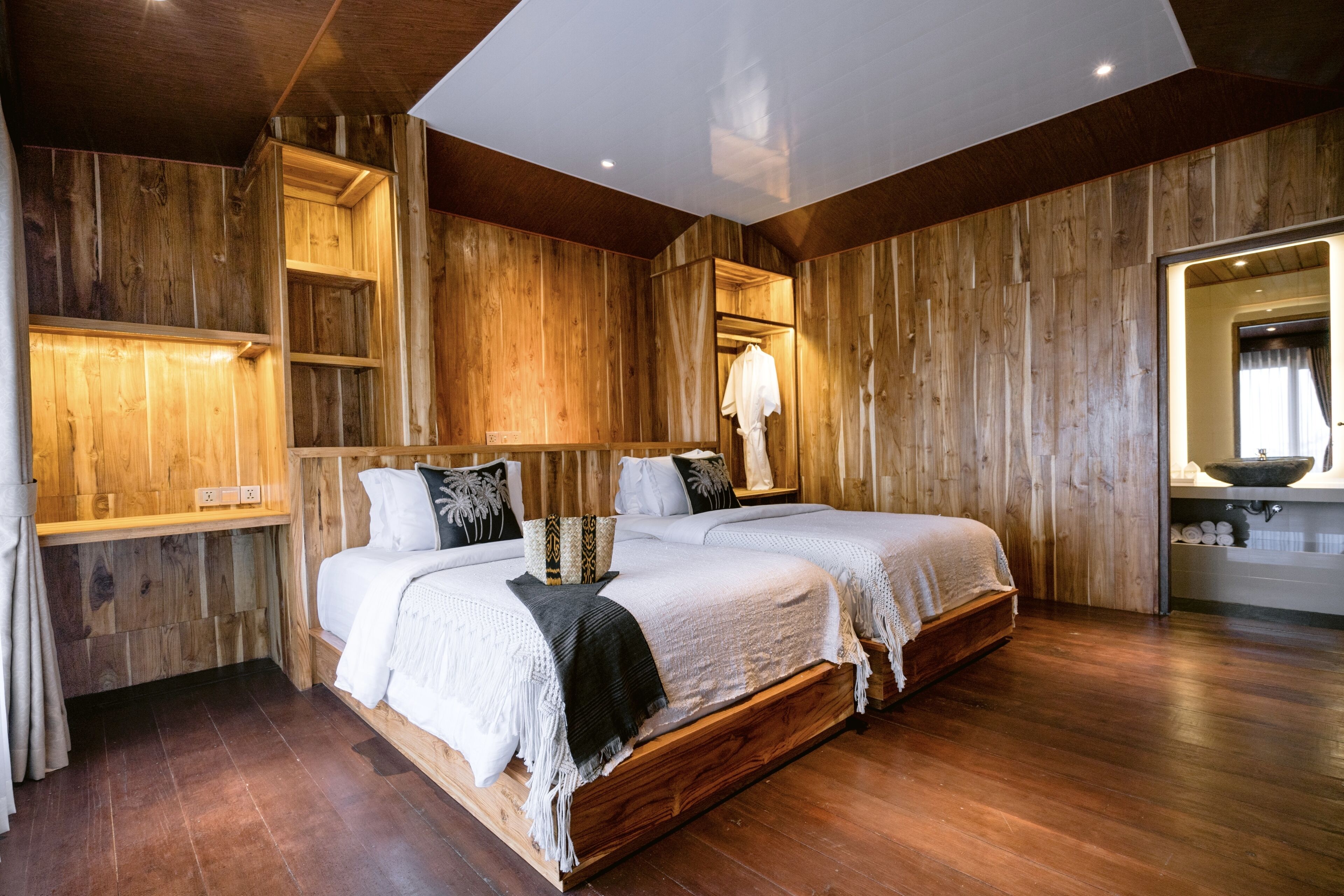 Habitación con paneles de madera, dos camas, estante de madera, espejo y lavamanos.