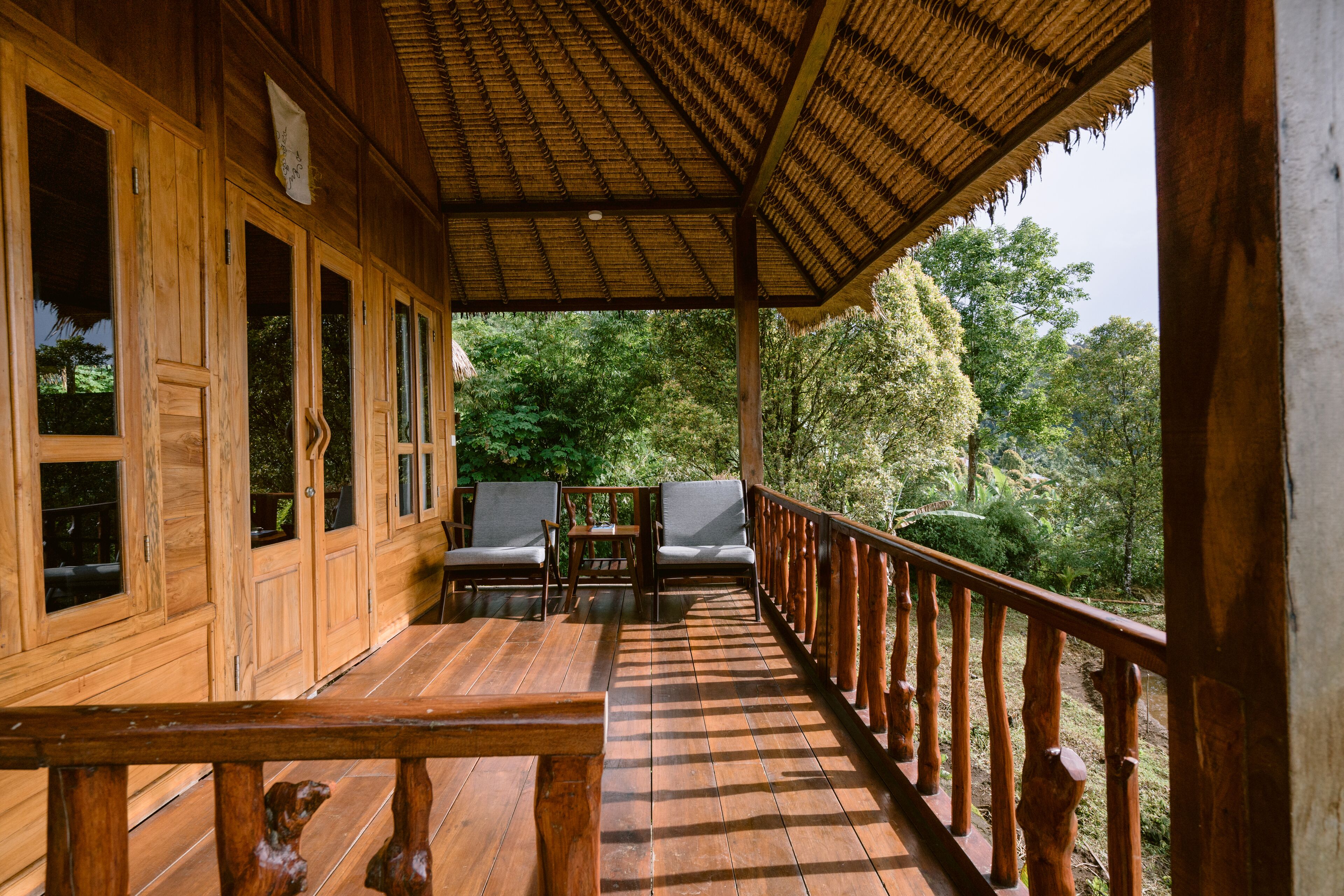 A wooden deck with a thatched roof, wooden railings, and two chairs.