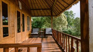 A wooden deck with a thatched roof, wooden railings, and two chairs.