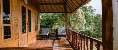 A wooden deck with a thatched roof, wooden railings, and two chairs.