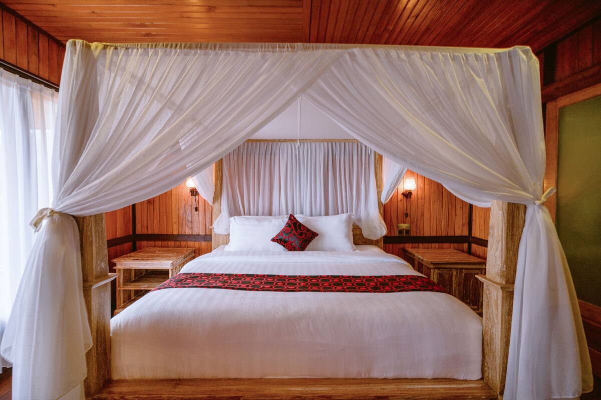 A bed with a canopy, wooden headboard, bedside tables, and a red patterned bedspread.