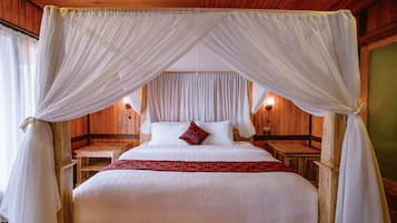 Cama con dosel, cabecera de madera, mesitas de noche y colcha estampada roja.