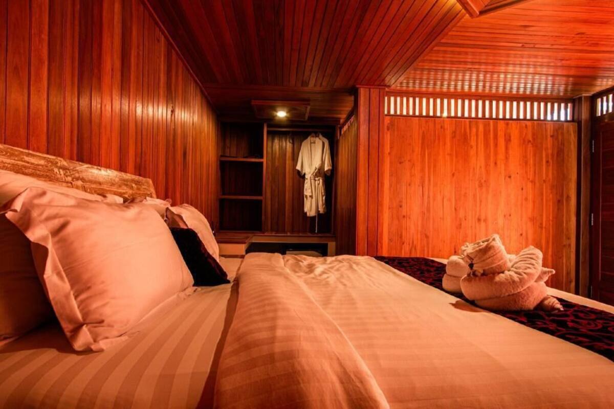 A wooden room with a bed, a robe hanging on a rack, and a towel on the floor.