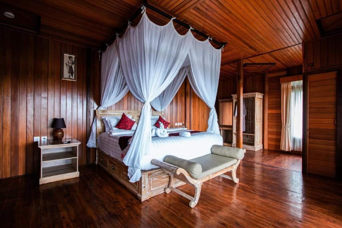 A wooden room with a four-poster bed, a bedside table, and a bench.