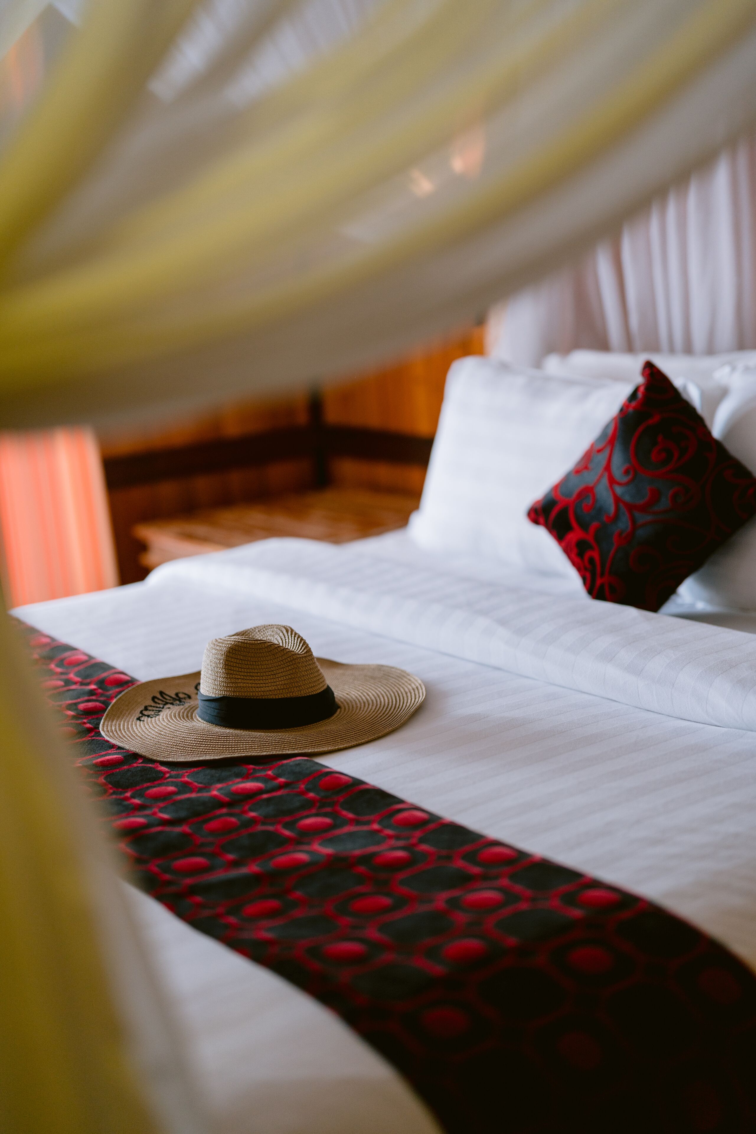 Un lit avec un chapeau de paille, une couvre-lit à motifs rouges et noirs, et un oreiller rouge et noir.