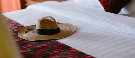 Un lit avec un chapeau de paille, une couvre-lit à motifs rouges et noirs, et un oreiller rouge et noir.