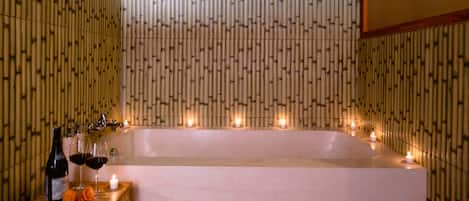 Un cuarto de spa con una bañera grande, velas y una mesa de madera con botellas y copas.