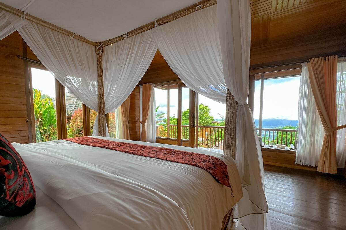 A bedroom with a large bed, white curtains, and a view of the outdoors.