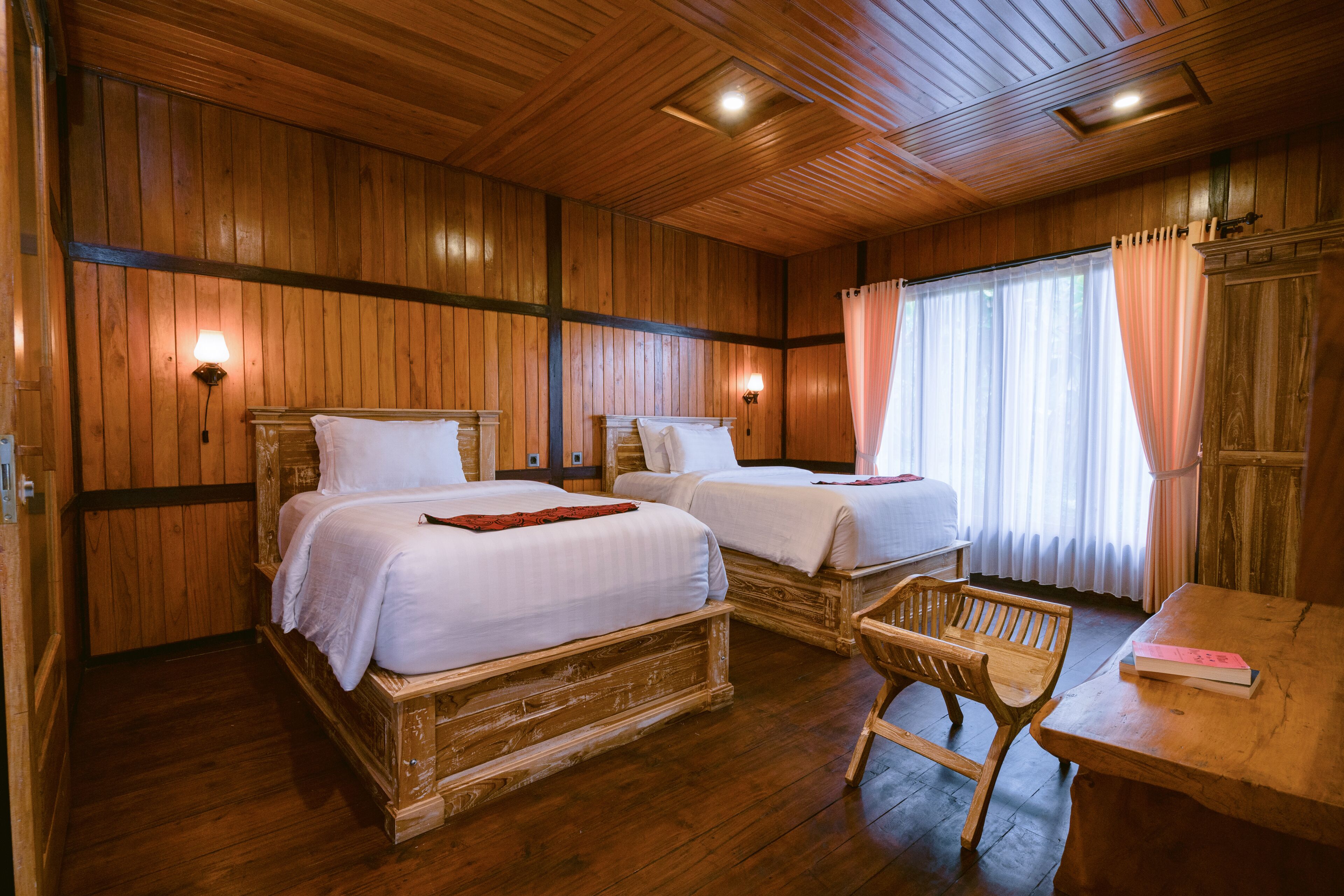 Een kamer in houtstijl met twee bedden, een houten stoel en een tafel met een boek.