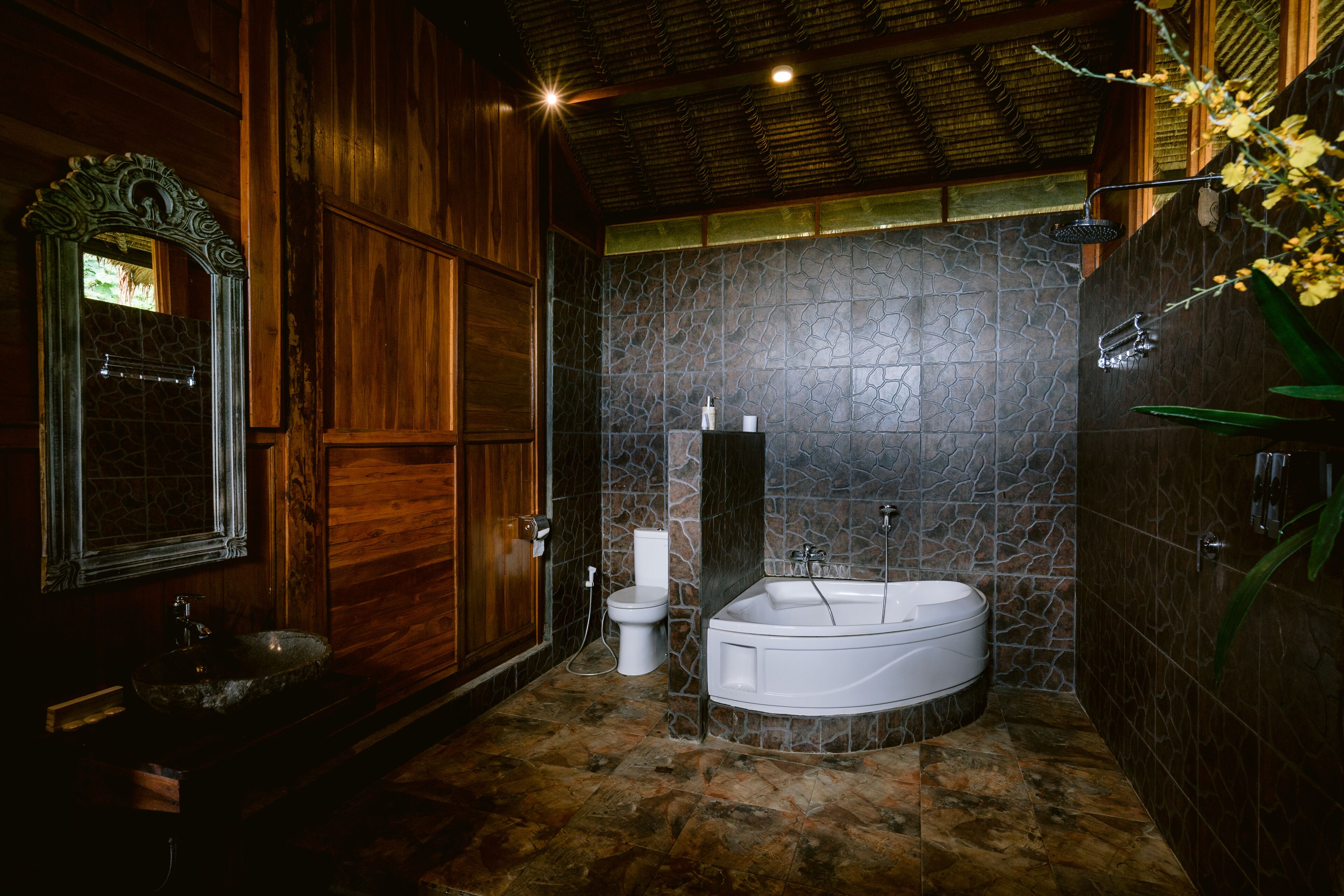 A bathroom with a stone wall, a wooden door, a sink, a toilet, and a bathtub.