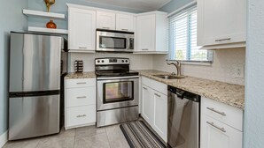 A modern kitchen with stainless steel appliances, white cabinetry, and a granite countertop. - Beautiful downtown Melbourne Beach renovated apartment one block from the beach! (Melbourne Beach)