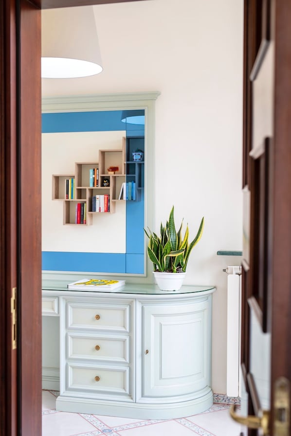 Canto de um quarto com um armário branco, uma planta em vaso e uma parede azul com estante.