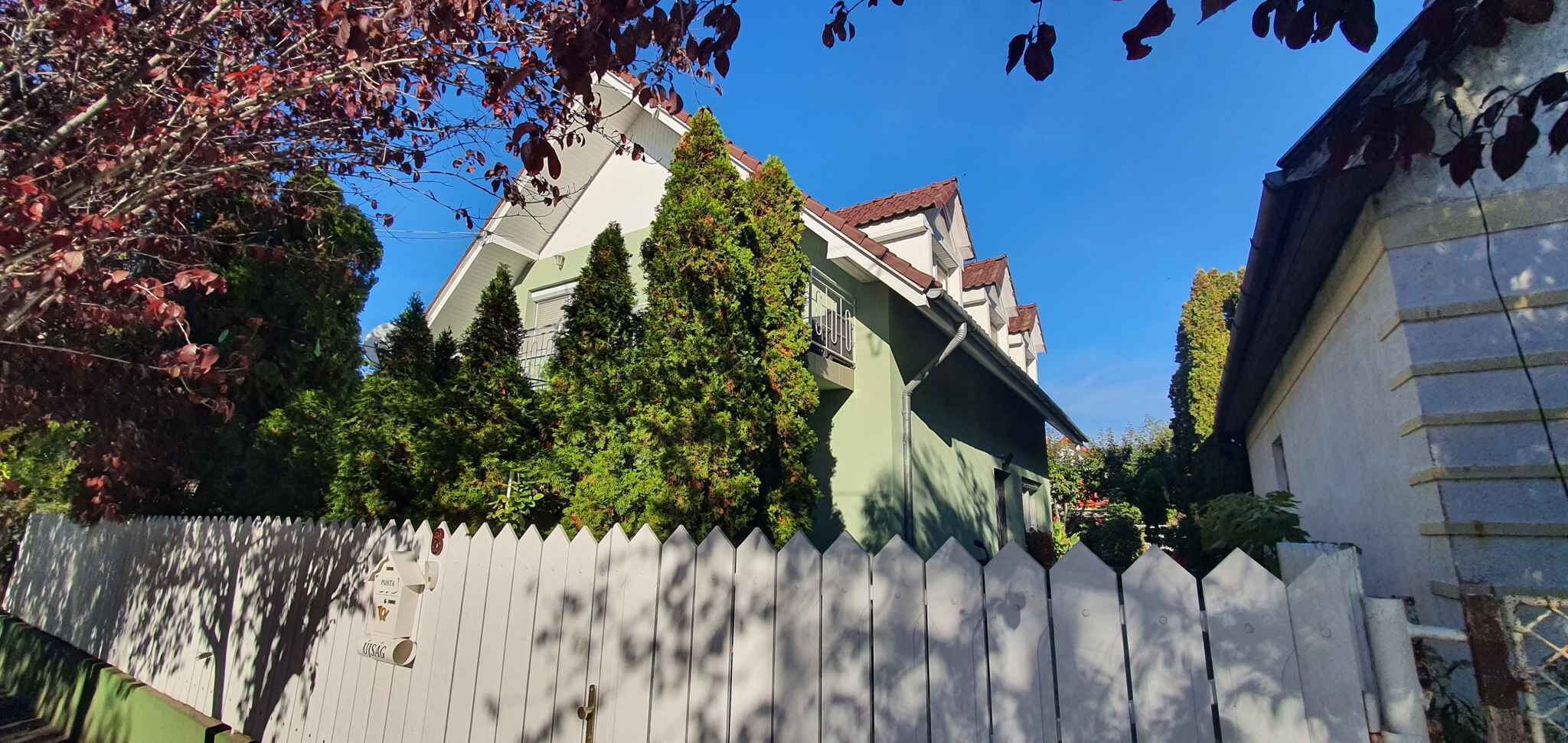Un edificio residenziale con facciata verde, numerose finestre e un recinto di legno bianco.