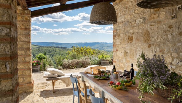 En rustik stenguldt bygning med et træbord dækket til spisning, med udsigt over et naturskønt landskab.
