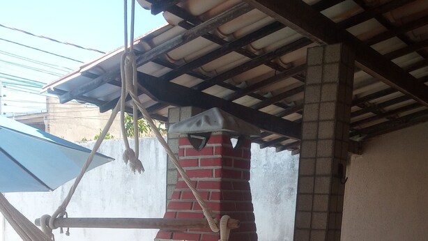 Eine Hängematte unter einer Holzpergola mit einem Kamin aus Backsteinen und einer weißen Wand im Hintergrund.