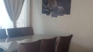 Ein Essbereich mit einem weißen Tisch, braunen Stühlen und einem an der Wand hängenden Bild eines Löwen.