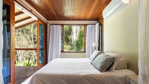 Un dormitorio con una cama grande, techo de madera y vistas a árboles a través de la ventana.