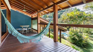 Una terraza de madera con una hamaca, piscina y exuberante follaje al fondo.