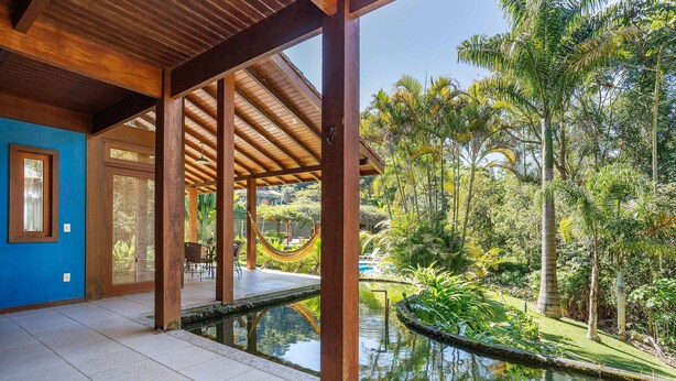 Un espacio al aire libre cubierto con piscina, vigas de madera y abundante vegetación.