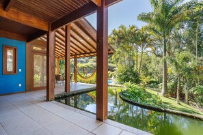 A covered outdoor area with a pool, wooden beams, and lush greenery.