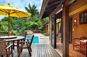 A wooden deck with a pool, outdoor seating, and a yellow umbrella.