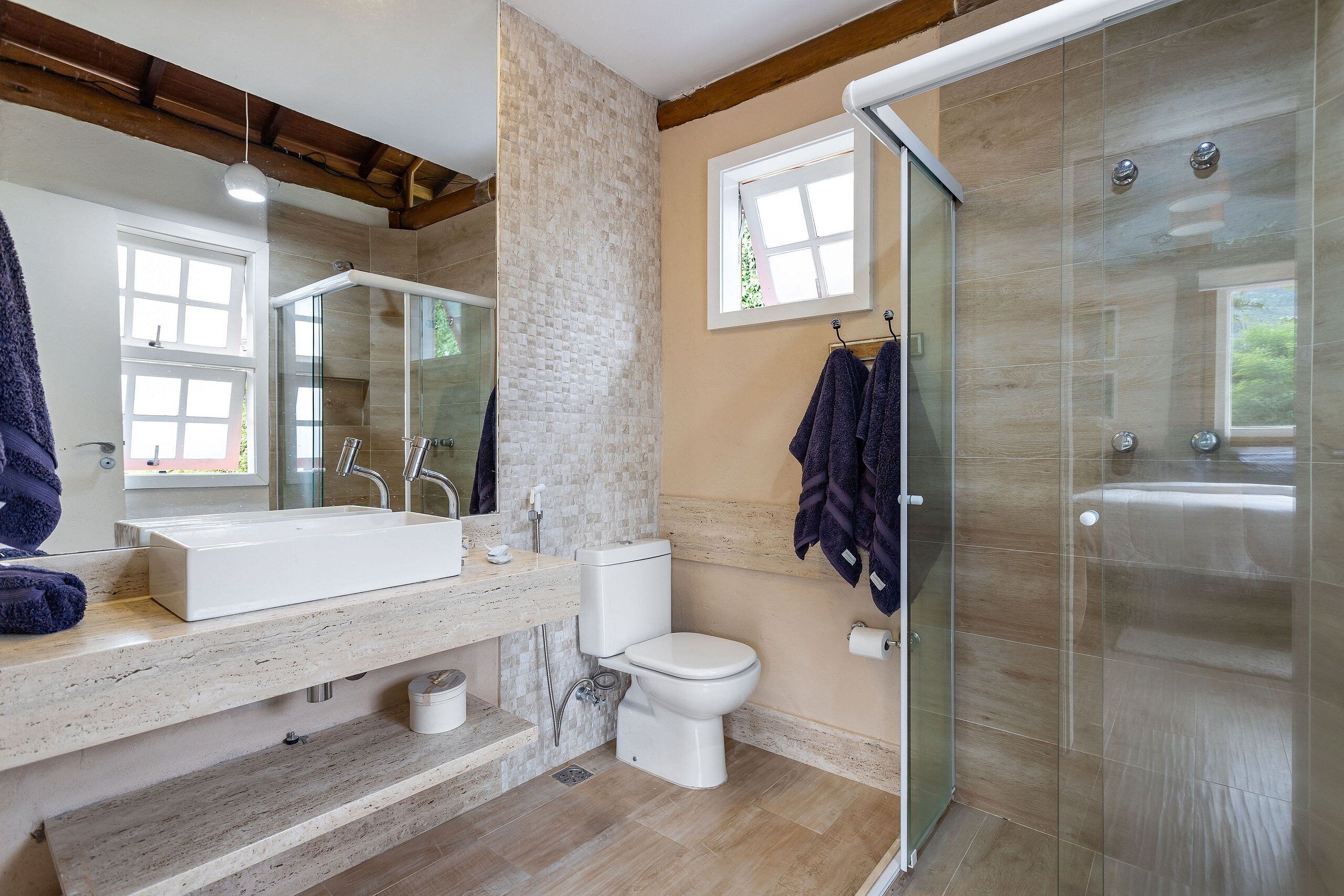 A modern bathroom with a large mirror, a white sink, a toilet, and a glass-enclosed shower.