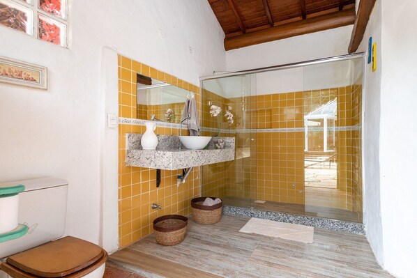 Un baño con cabina de ducha de vidrio, un lavamanos con encimera de mármol y un inodoro con asiento marrón.