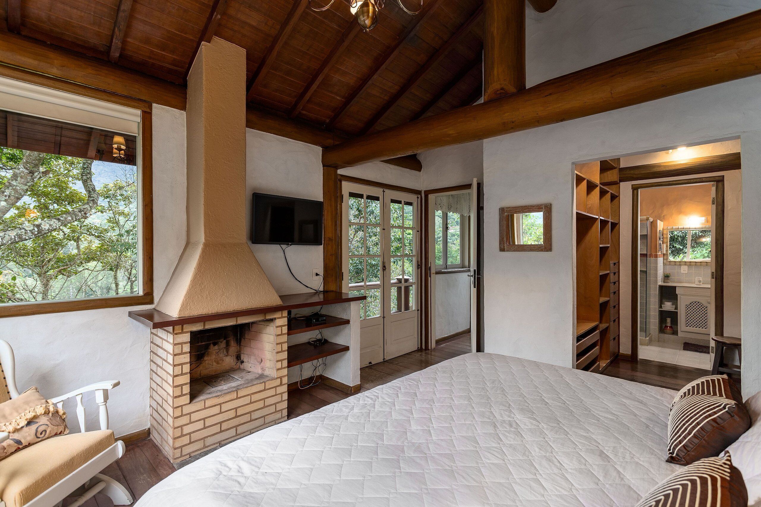 Un dormitorio con chimenea de ladrillo, una cama, un televisor y vistas al exterior.