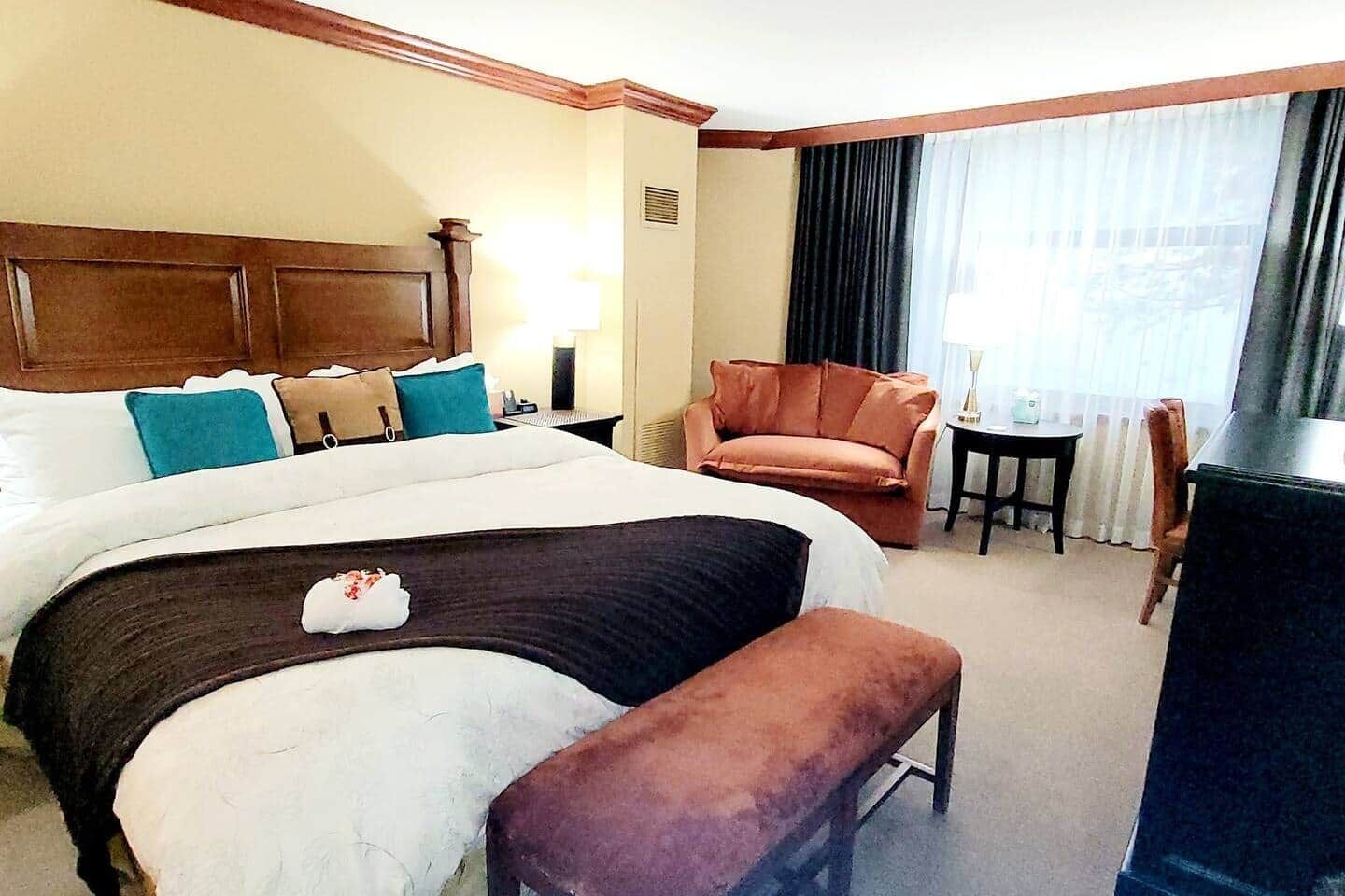 A hotel room with a large bed, a wooden headboard, a brown armchair, a small table, and a desk.