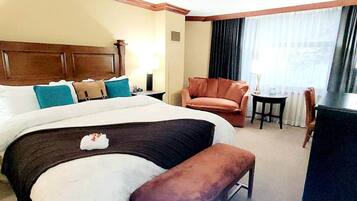 A hotel room with a large bed, a wooden headboard, a brown armchair, a small table, and a desk.