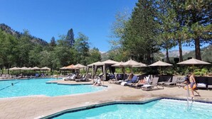 A pool area with lounge chairs and umbrellas, surrounded by trees and a mountainous backdrop.
