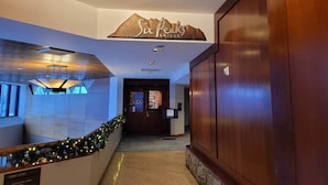 A hotel lobby with a reception desk, a sign for 'Six Peaks Grille', and a staircase with a Christmas garland.