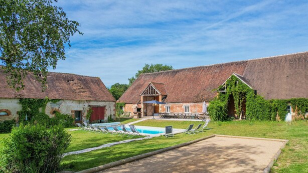 Un bâtiment de style traditionnel doté d’une piscine, de chaises longues et d’un court de tennis.