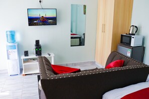 Habitación de hotel con cama, televisor montado en la pared, dispensador de agua, cafetera y microondas.
