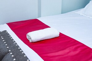 Una cama bien hecha con una almohada blanca y una toalla blanca enrollada.