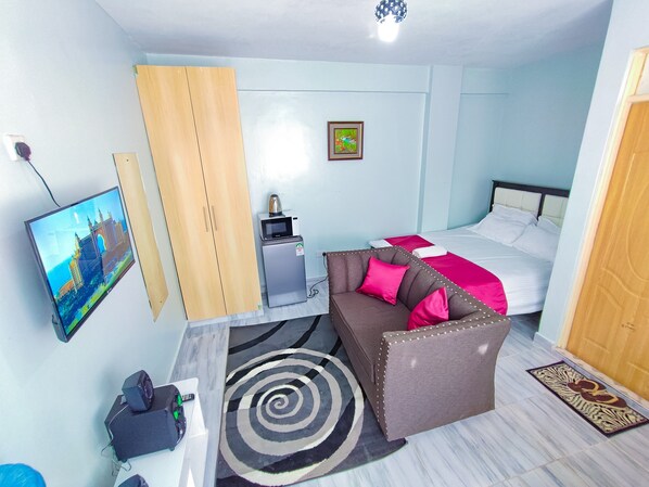 Una habitación de hotel con cama, sofá, televisión, un refrigerador pequeño y un escritorio con computadora.