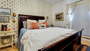 A neatly made bed with a wooden headboard, a bedside table with a lamp, and a colorful rug.