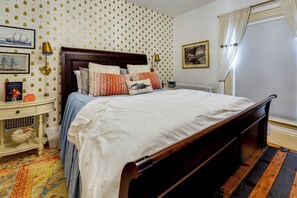 A neatly made bed with a wooden headboard, a bedside table with a lamp, and a colorful rug.