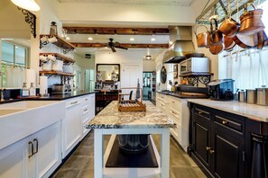 Una cocina moderna con armarios blancos, encimera de mármol y utensilios de cobre colgados.