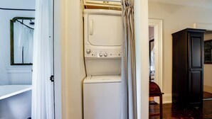 A laundry room with a front-loading washer and dryer, a wooden chair, and a dark wooden cabinet.