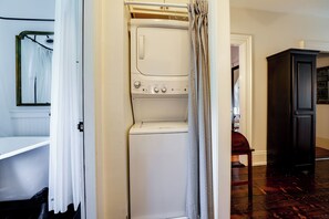 A laundry room with a front-loading washer and dryer, a wooden chair, and a dark wooden cabinet.