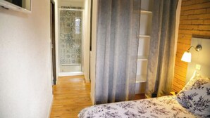 Une chambre avec un plancher en bois, un lit recouvert d’une literie à motifs floraux, une table de chevet avec une lampe et une fenêtre avec des rideaux.